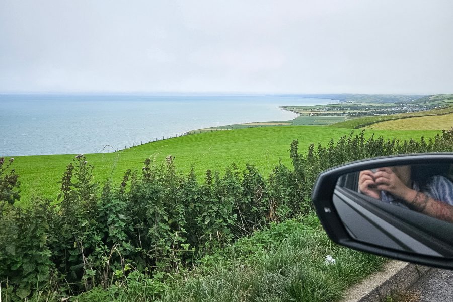 Writer leans out of a car window to take a photo of the Welsh coastline.