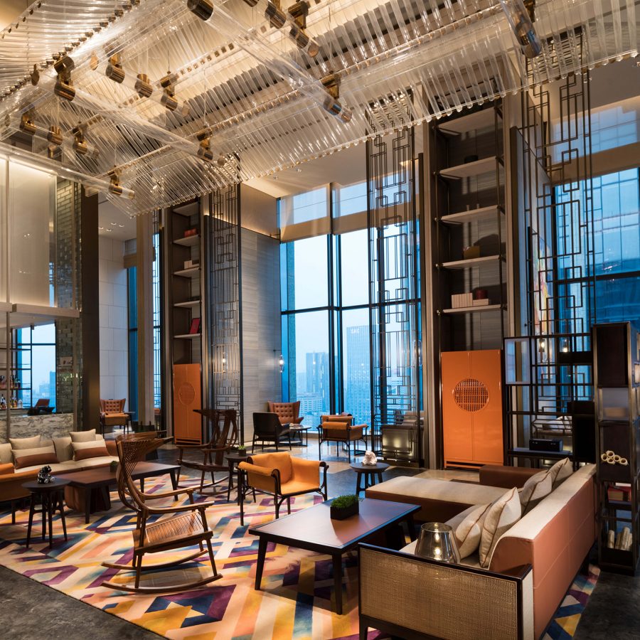 The interior of the lounge in Canopy by Hilton Chengdu City Centre features a double ceiling and wooden furniture. 