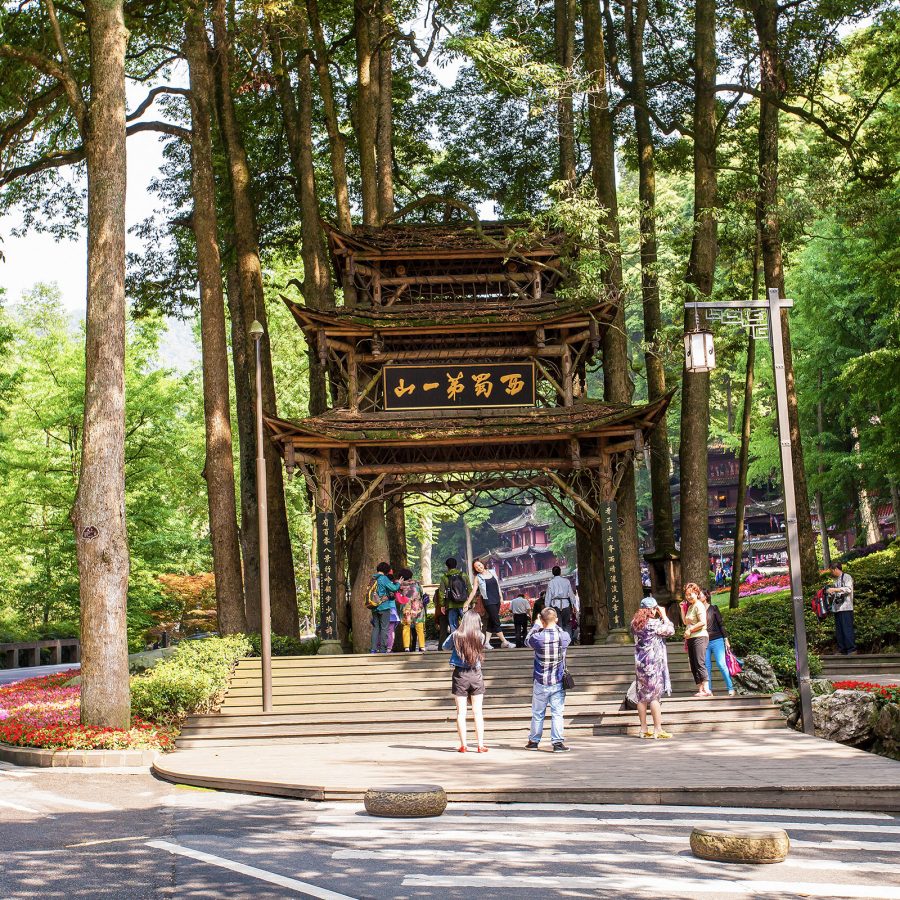 People take pictures of an entryway built in the middle of a forest, leading to a mountain trail in Chengdu. 