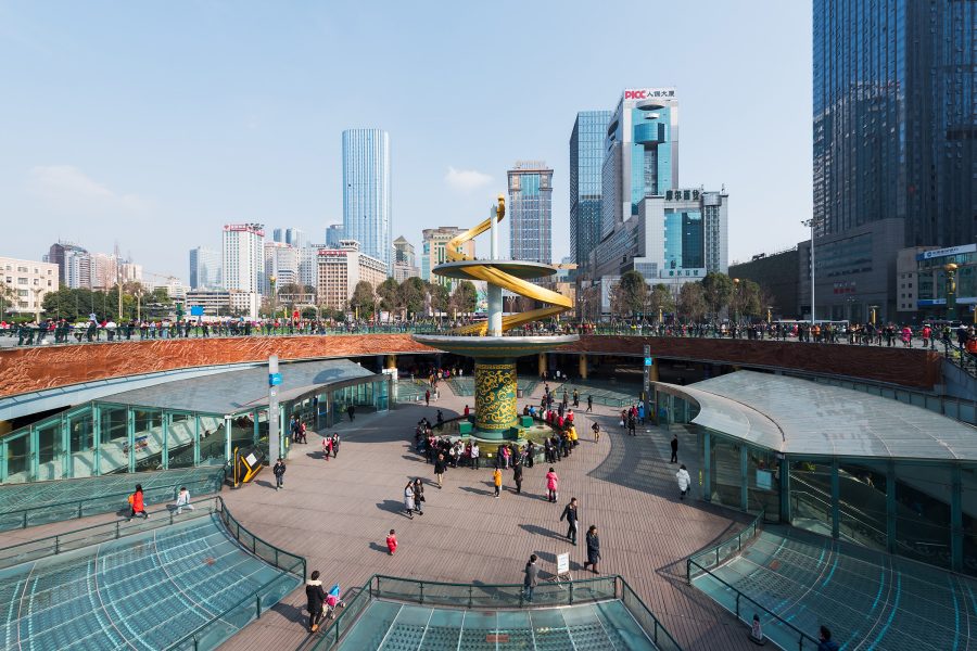A square with a sculpture in the middle is bordered by a subway station and office buildings in Chengdu.