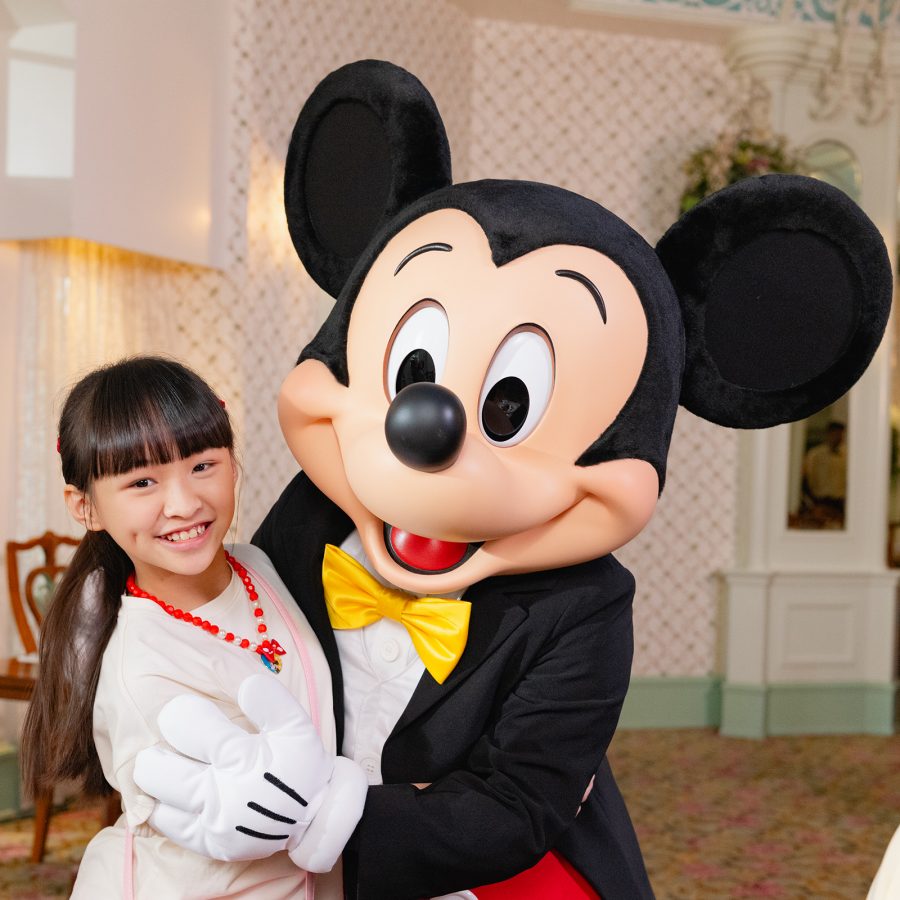 Mickey Mouse hugging a smiling girl at the Hong Kong Disneyland Hotel.
