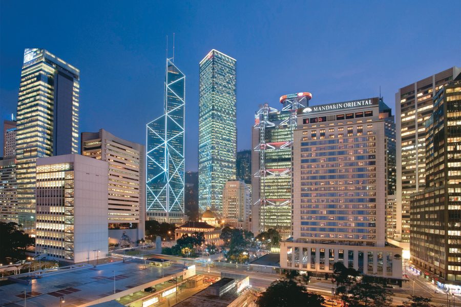 Exterior view of Mandarin Oriental Hong Kong building alongside Hong Kong’s other skyscrapers, illuminated at night. 