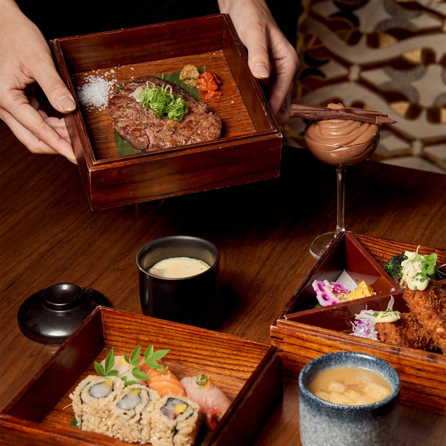 An assortment of delicate, colourful Japanese dishes are displayed in polished wooden boxes on a table. 