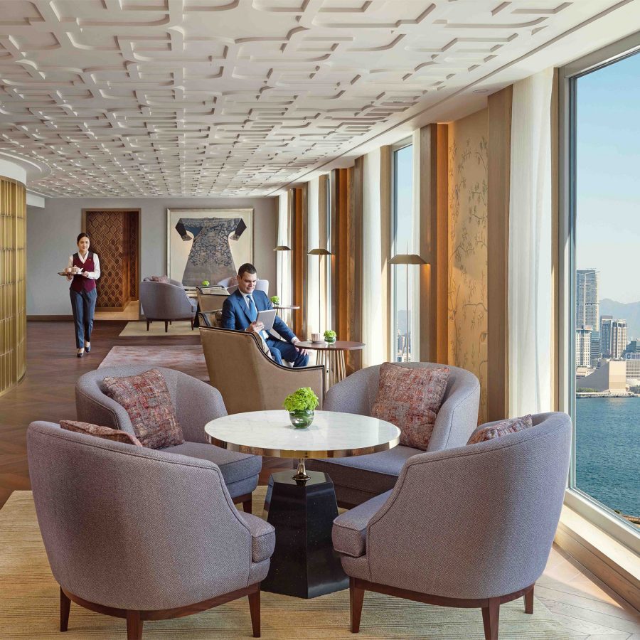 Interior of The Mandarin Club, a daytime lounge with purple lounge chairs arranged around marble tables, and floor-to-ceilings windows that look onto Victoria harbour. 