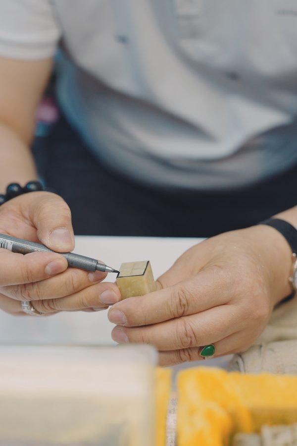 A close-up of a hand coating a stone Chinese seal with ink at an outdoor stall. 