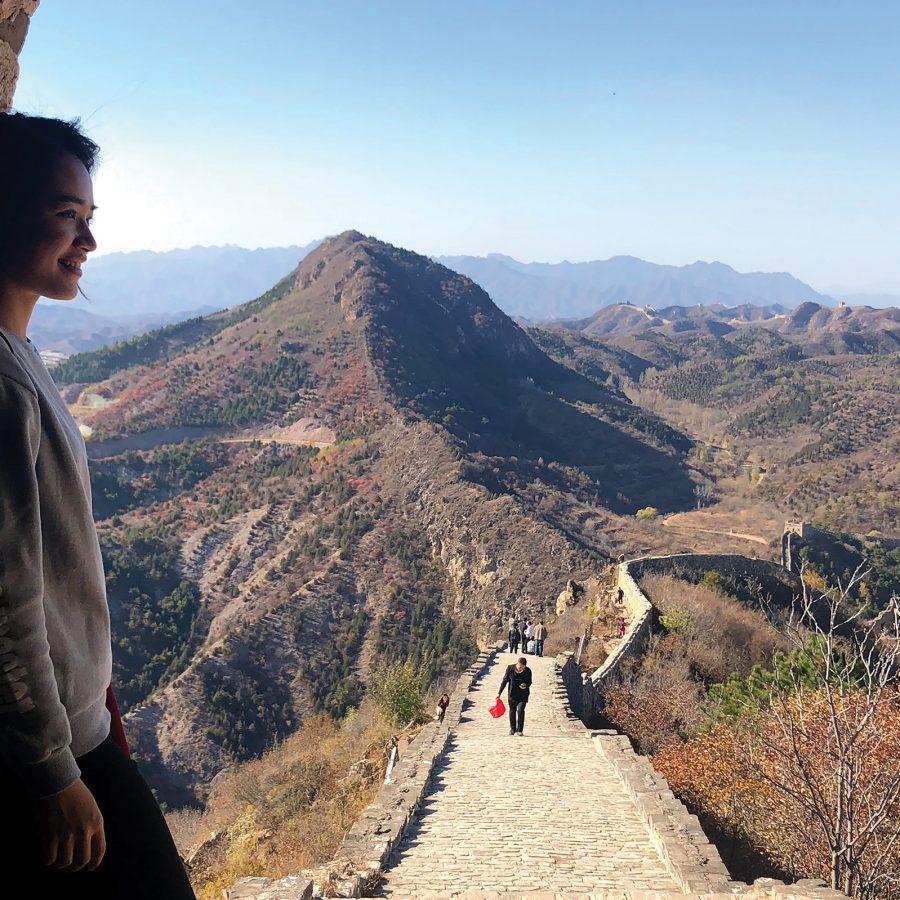 Cathay cabin crew Jade Cheng at the Simatai section of the Great Wall of China. The wall stretches behind her into the mountains, which stand out against a blue sky.