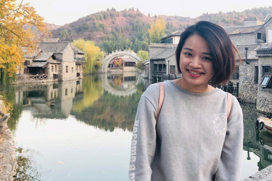 Cathay cabin crew Jade Cheng smiles while standing next to a river lined with traditional buildings in Gubei Water Town