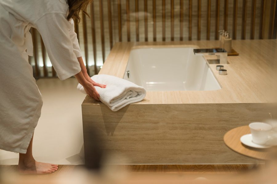 A woman folding a white towel by a bathtub with wooden frame at a Cathay Pacific lounge.
