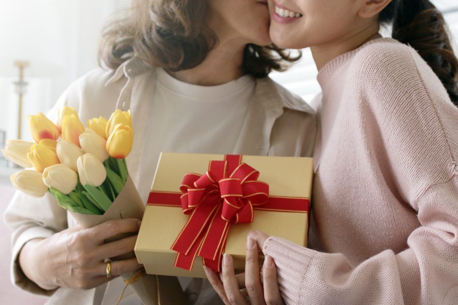 A mother kisses her daughter on the cheek after being presented with a bouquet of tulips and a gift box.