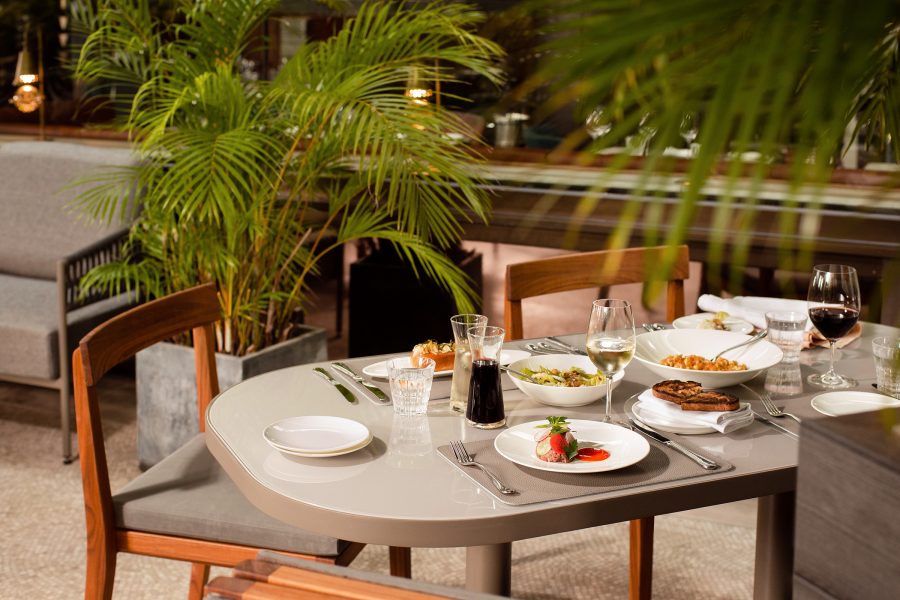 The interior of The Continental features simple furniture and green plants, including a dining table filled with Western dishes and wine glasses.