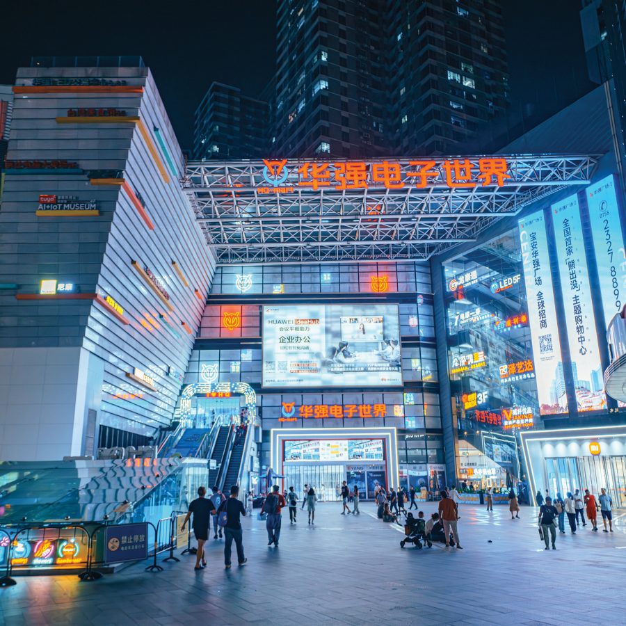 An exterior view of Huaqiangbei Electronics Market building at night while people walk around.