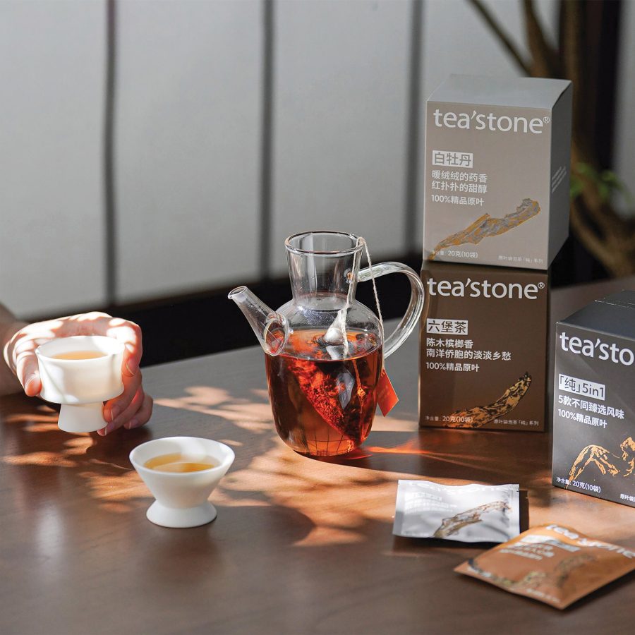 A closeup of Chinese tea in a glass pot and ceramic cups next to Tea’stone products.