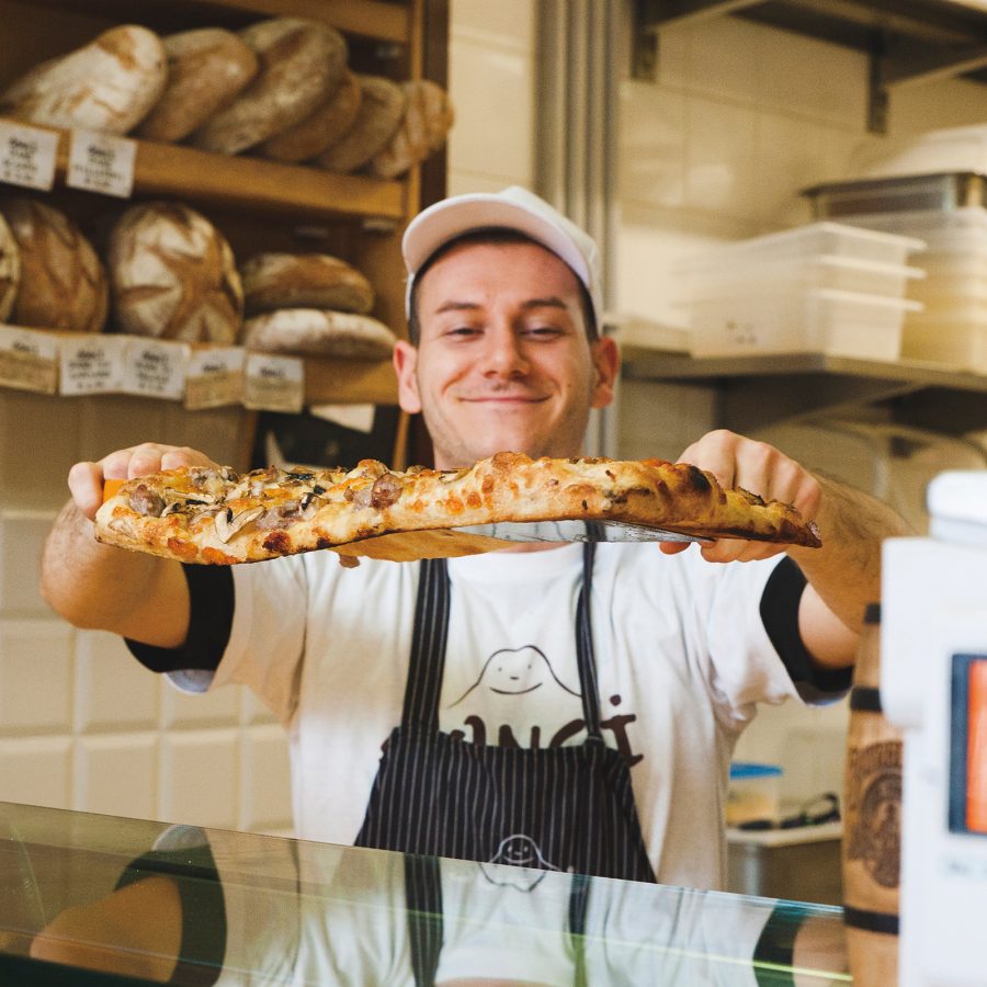 A man holds up a pizza from Bonci Pizzarium in Rome.