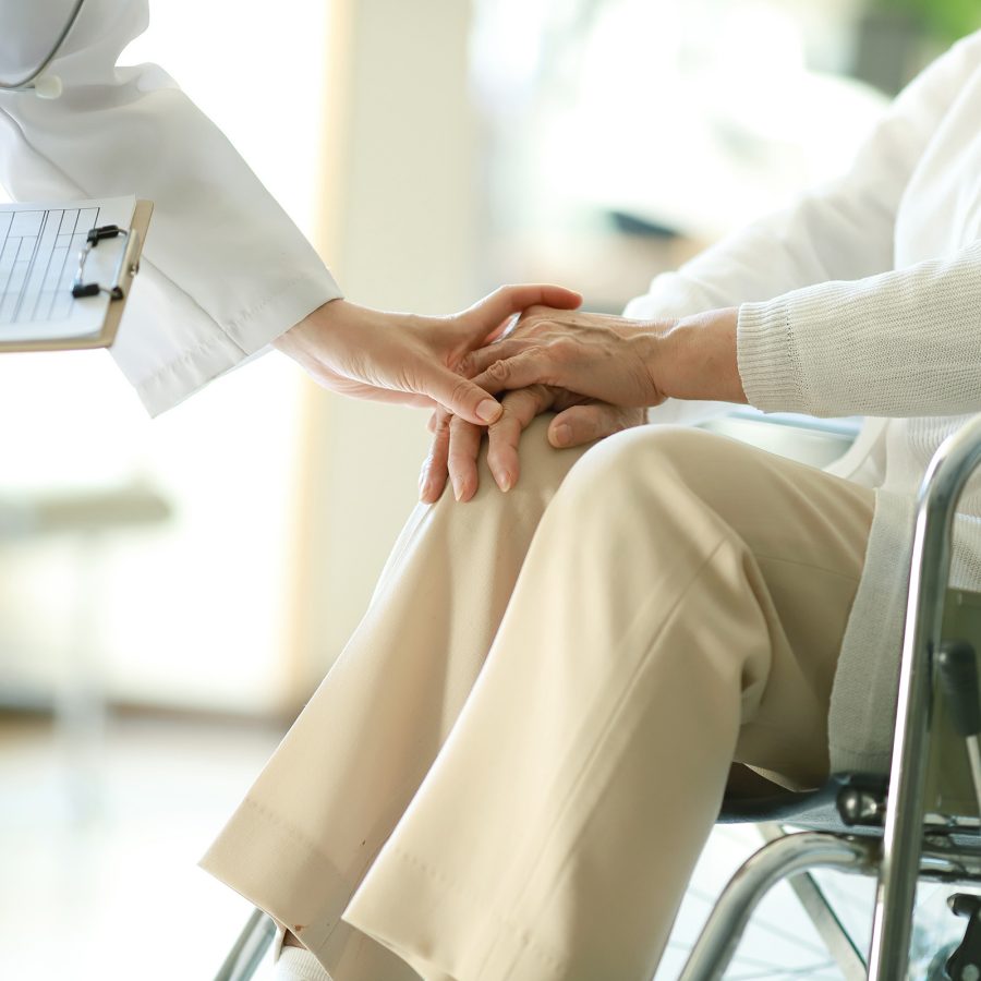 Close-up of a doctor holding a patient's hand in a wheelchair.