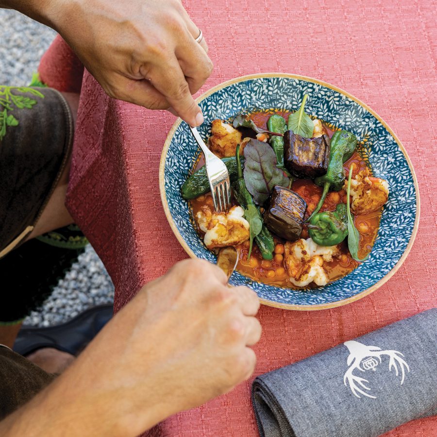 A closeup of hands holding a silver fork and spoon digging into a saucy German dish at Hirschgarten in Munich, Germany