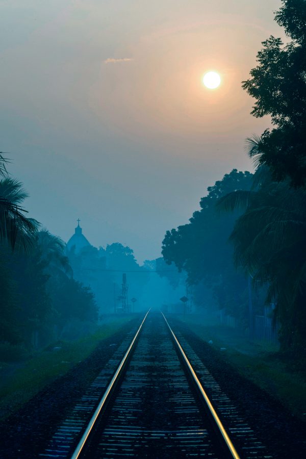 A foggy view of railroad tracks flanked by trees and a view of the sun in the sky in North Sri Lanka.