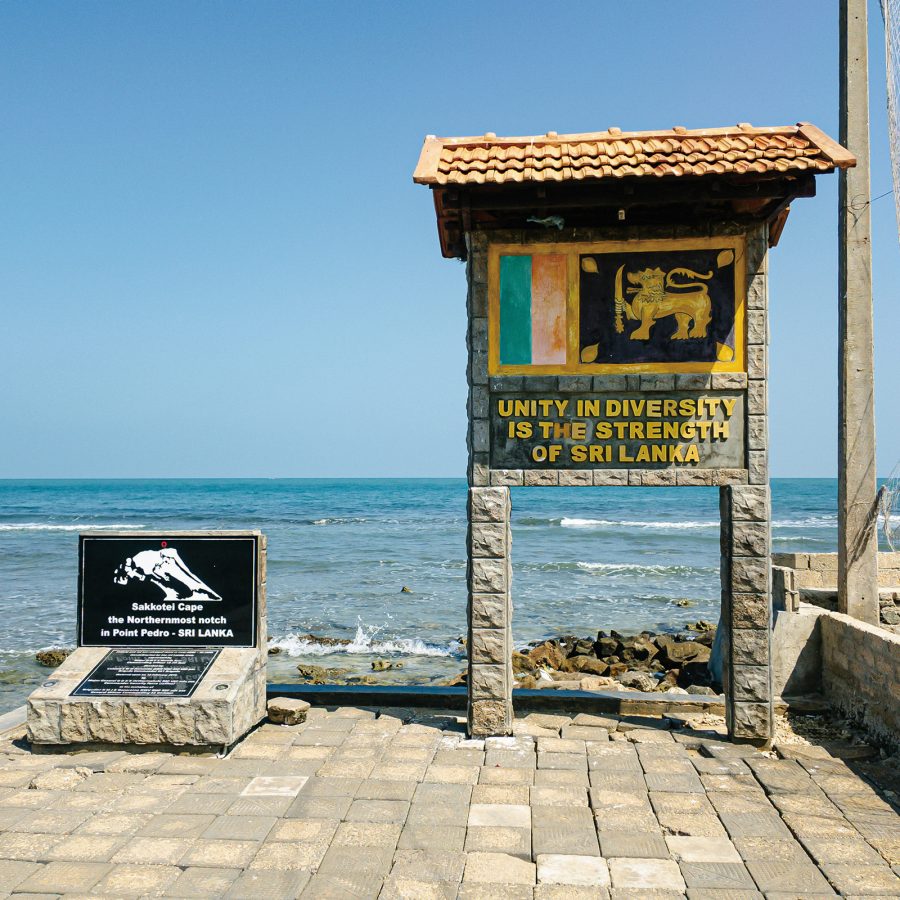 A view of a stone signpost with the Sri Lankan flag by Pedro Beach with the view of blue sea and sky in the background