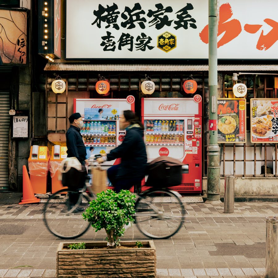 Person rides a bike past two Japanese vending machines.