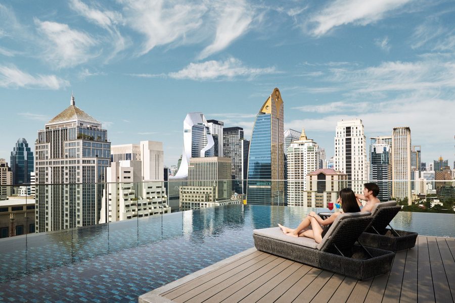 A man and a woman in swimsuits lounge by the Horizon Pool at the Sindhorn Midtown Hotel Bangkok on a sunny day.