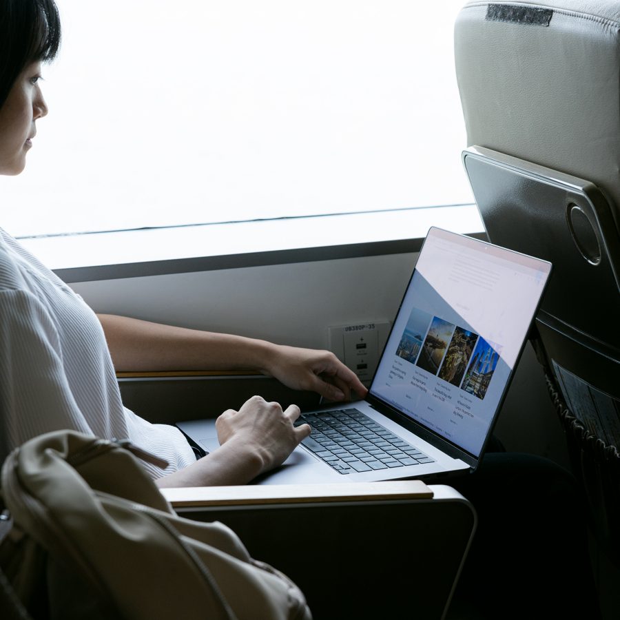 A passenger looks at their laptop screen while seated next to a window on board the ferry.