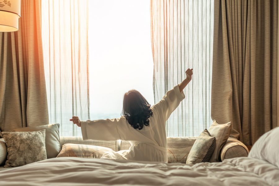 A woman in a bathrobe stretching in her hotel room. 