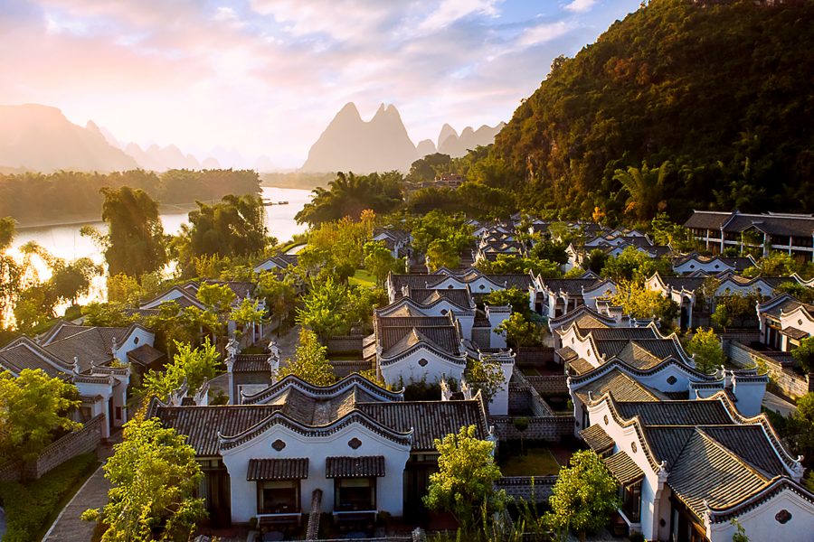 Villas at Banyan Tree Yangshuo surrounded by trees, with majestic mountains in the background. 