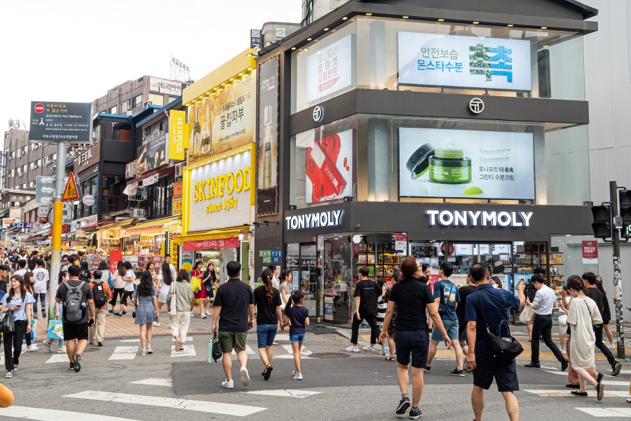 People walking on a street in Hongdae with shops like TONYMOLY and SKINFOOD.