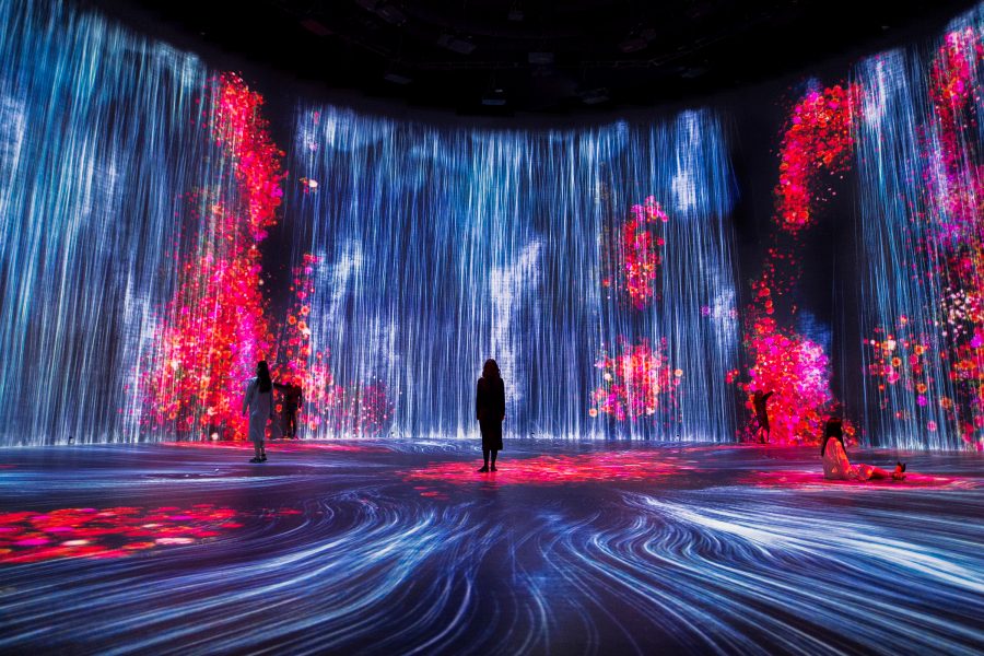 People standing in a dark room with a large digital art installation in Tokyo’s TeamLab Borderless.