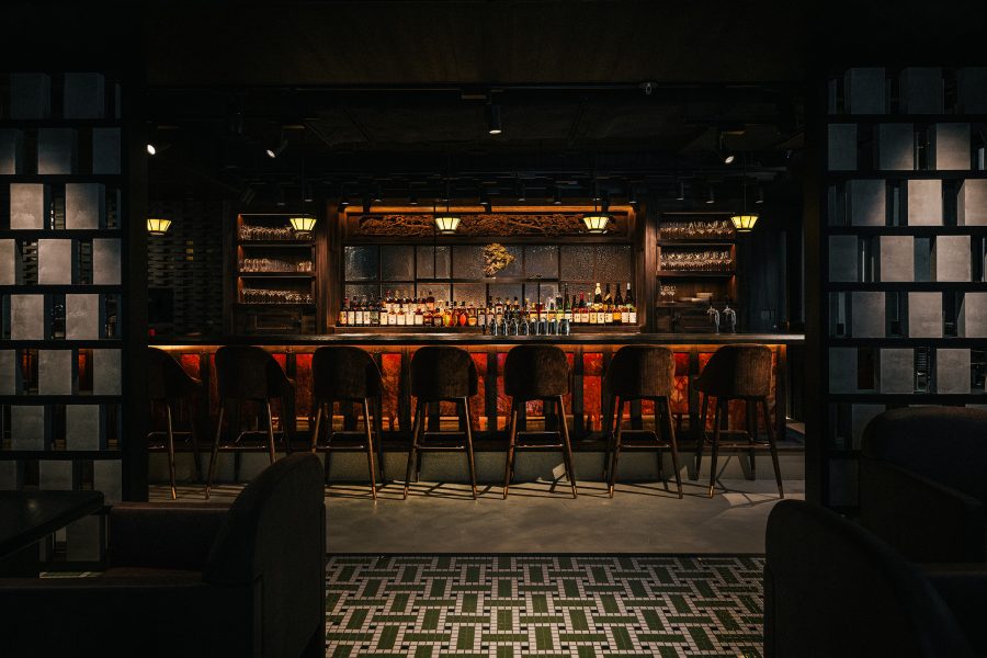 Bar seating at Gokan is lit up by overhead lights, while behind it are features like green patterned floors and low chairs.