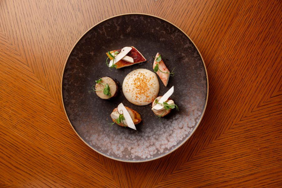 From above, a brown dish is topped with various bites garnished with greens. You’ll find this dish at three Michelin-starred Amber in Hong Kong.