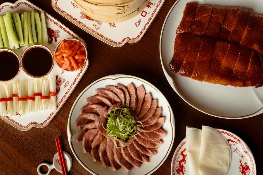 From above, a spread of Cantonese dishes including Peking duck wraps and chilled meat covers a tabletop.