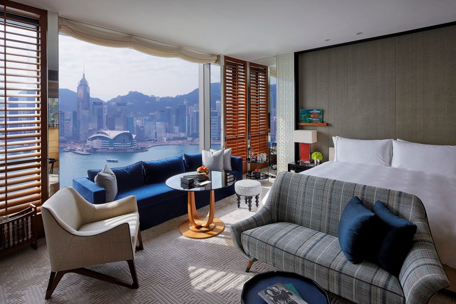 A guest room at Rosewood Hong Kong has a bed, plush seating and a panoramic view of the city’s skyline.