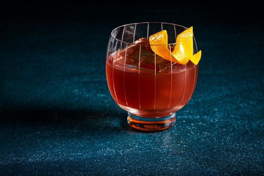 A mahogany-coloured cocktail with a curl of orange peel sits on a blue counter at 42 Mayfair in London