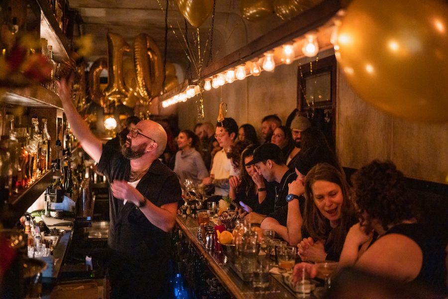 Customers chat as a bartender reaches for something behind the bar at Attaboy in New York