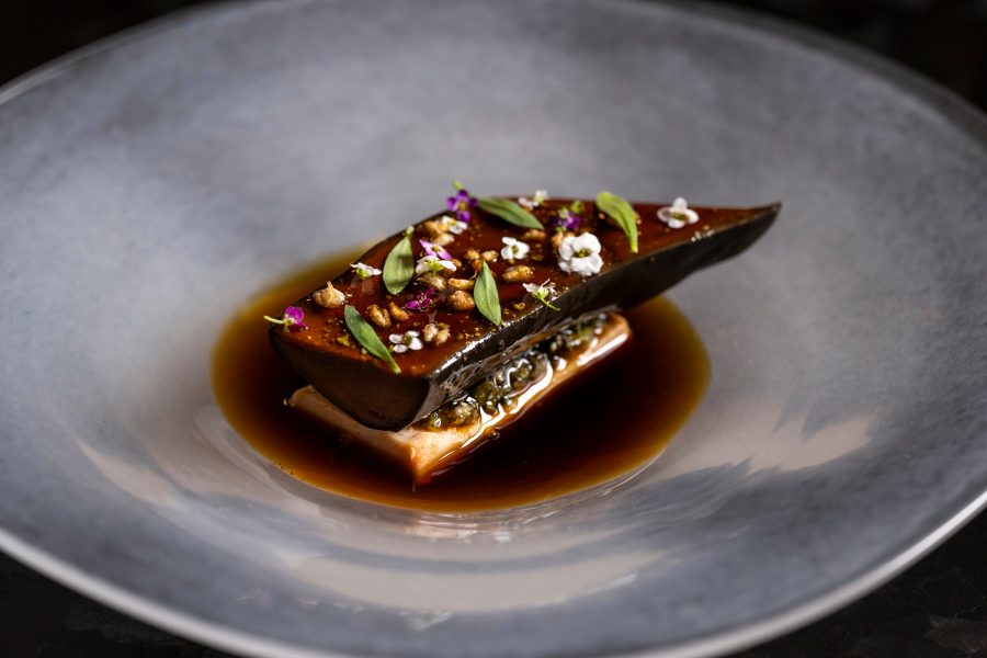 A grey plate with a dish decorated in small flowers and leaves served at Atomix in New York City
