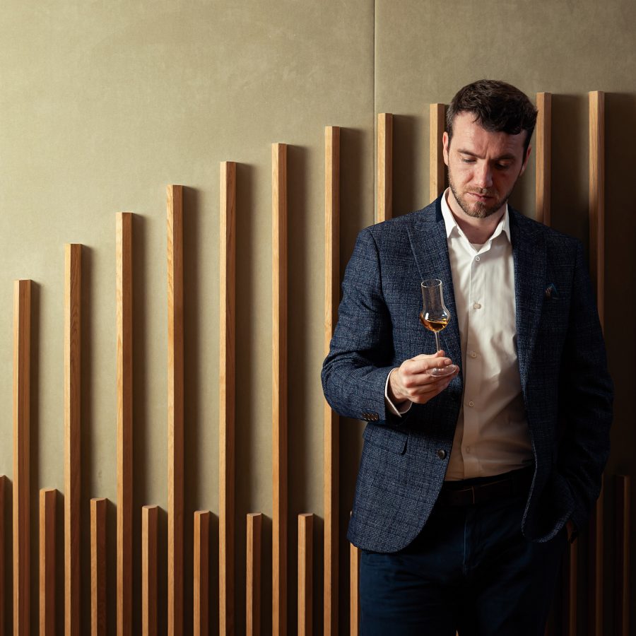 Euan Kennedy observing a glass of whisky against an abstract wooden backdrop.