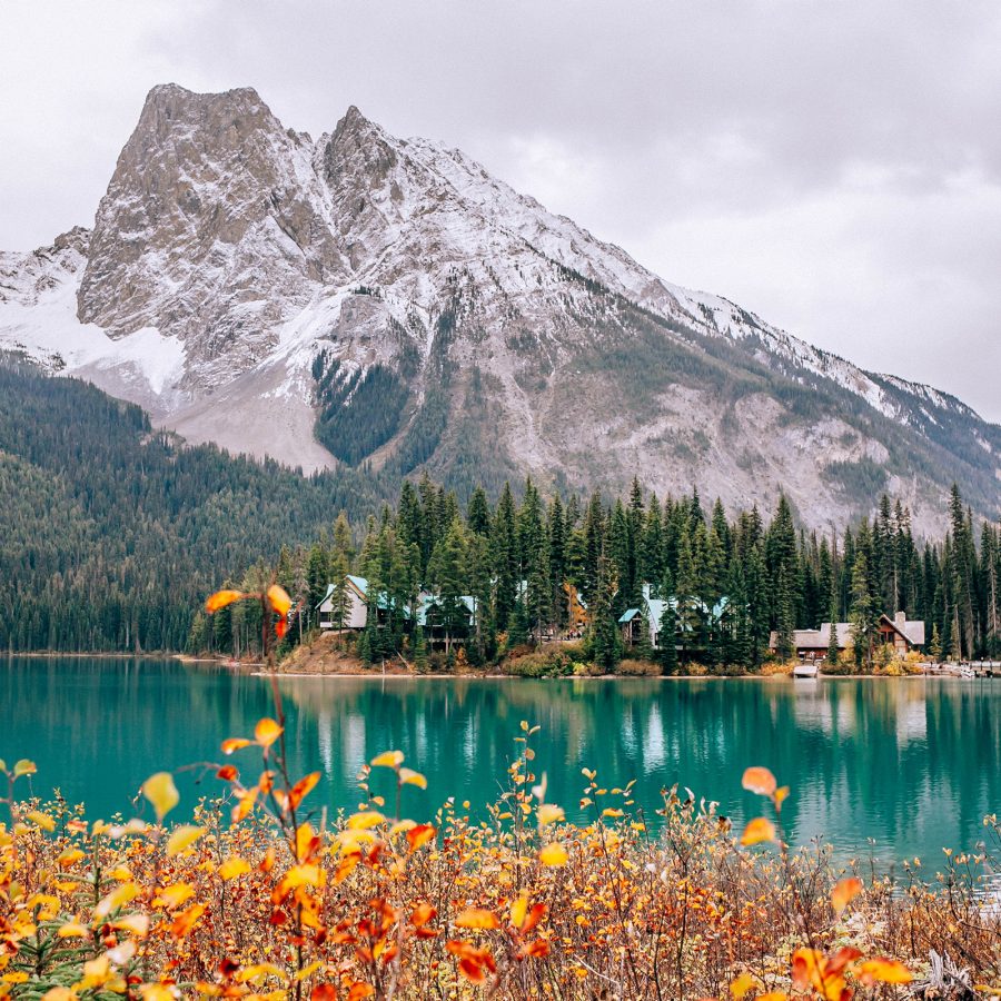 Exterior view of The Emerald Lake Lodge, with the crystal-clear lake in the foreground and snowy mountains in the background.