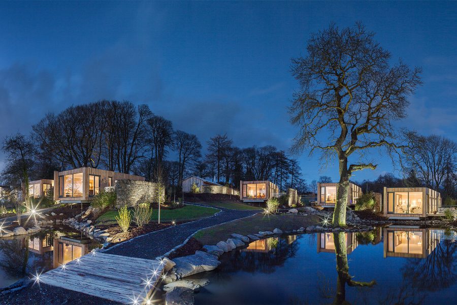 Exterior view of multiple cabins at night, with water in the foreground.