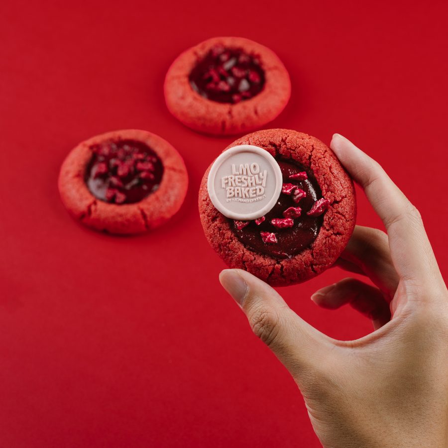  A hand holds up a red cookie with red filling at LMO Freshly Baked.