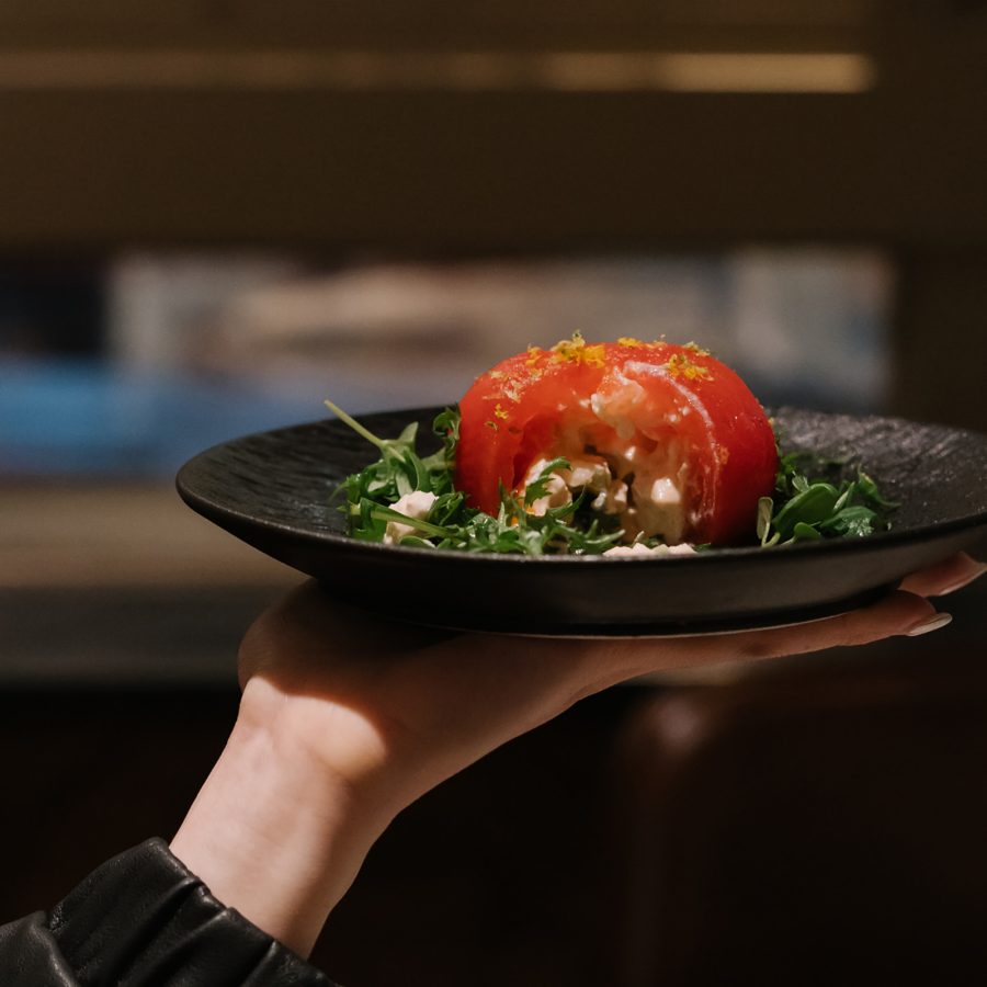 A waiter holds up a dish with the shop’s interior in the background. 