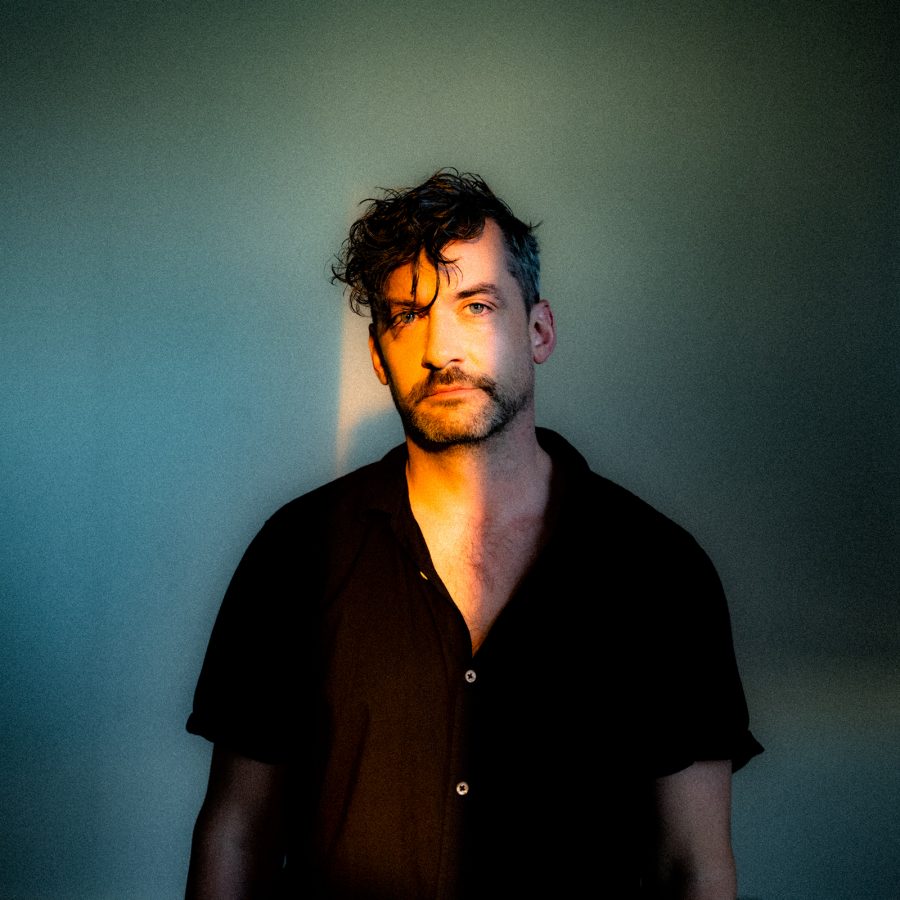 Bonobo standing against a blank wall with light illuminated across his face. 