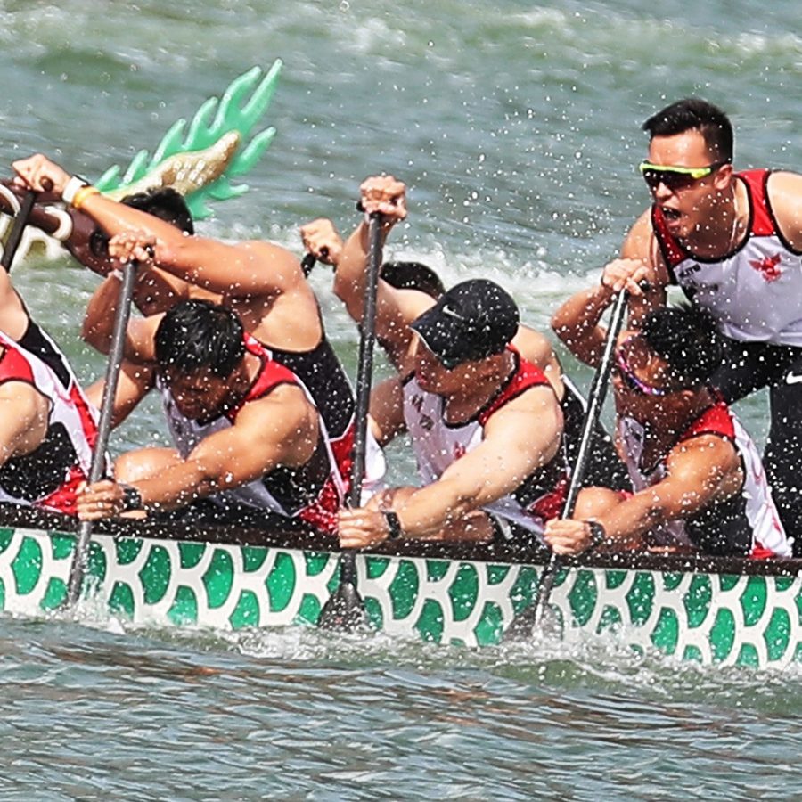 A team of male dragon boat racers paddle hard over the water. 
