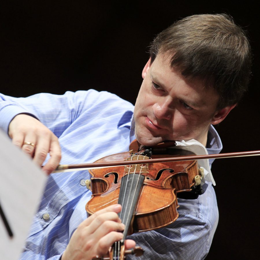 Frank Peter Zimmermann plays the violin as he glances at his sheet music on a music stand. 