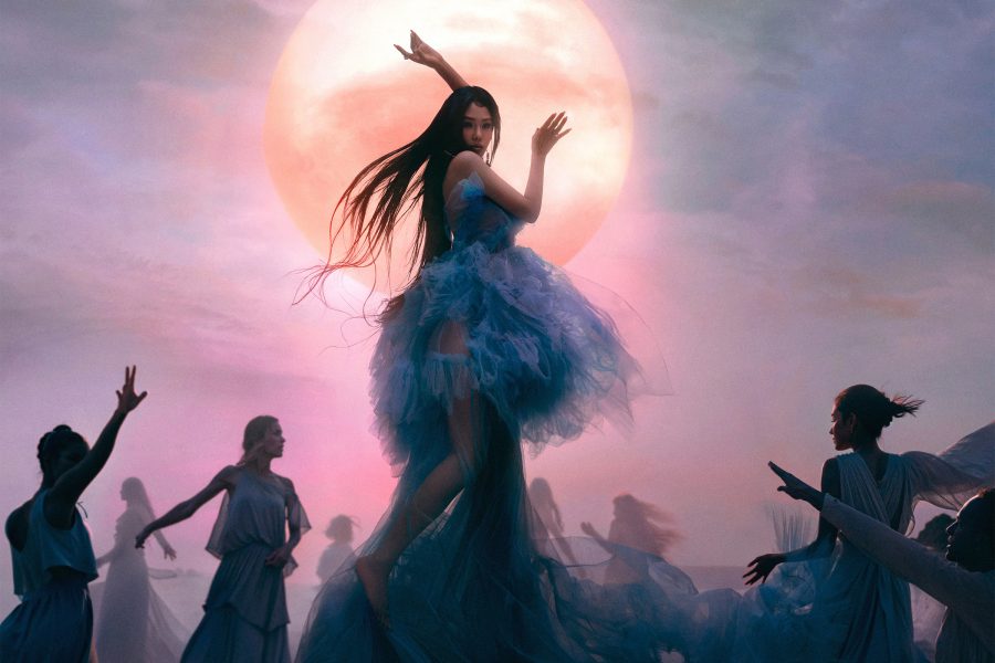Woman in a tulle dress and flowing hair dances before a backdrop of the moon and purple night sky.