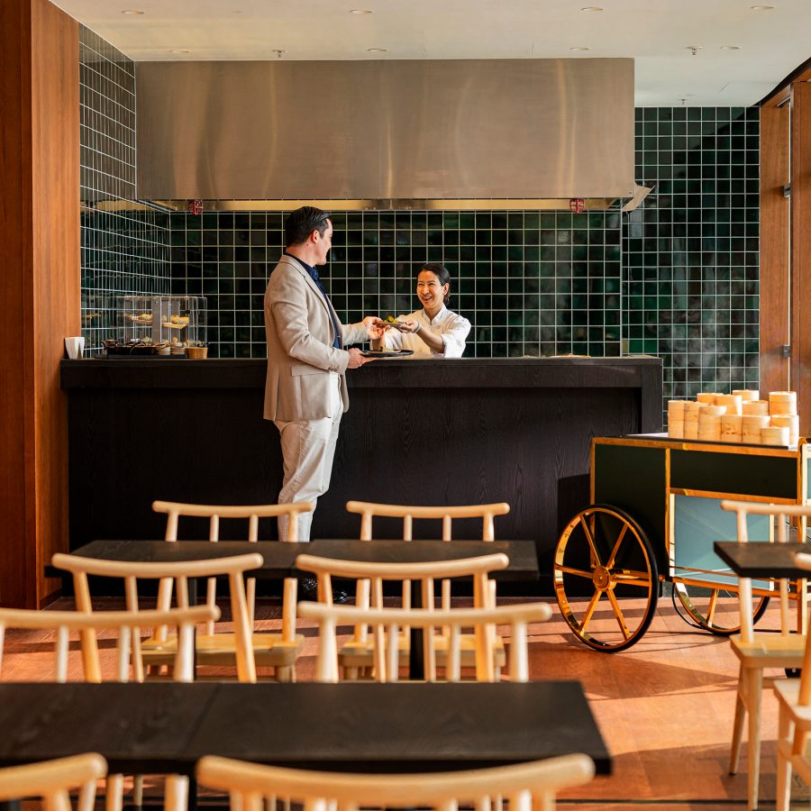 A customer speaks to a staff member at The Nook, a dining area inside The Bridge decorated with green tiled walls, simple furniture and plants.