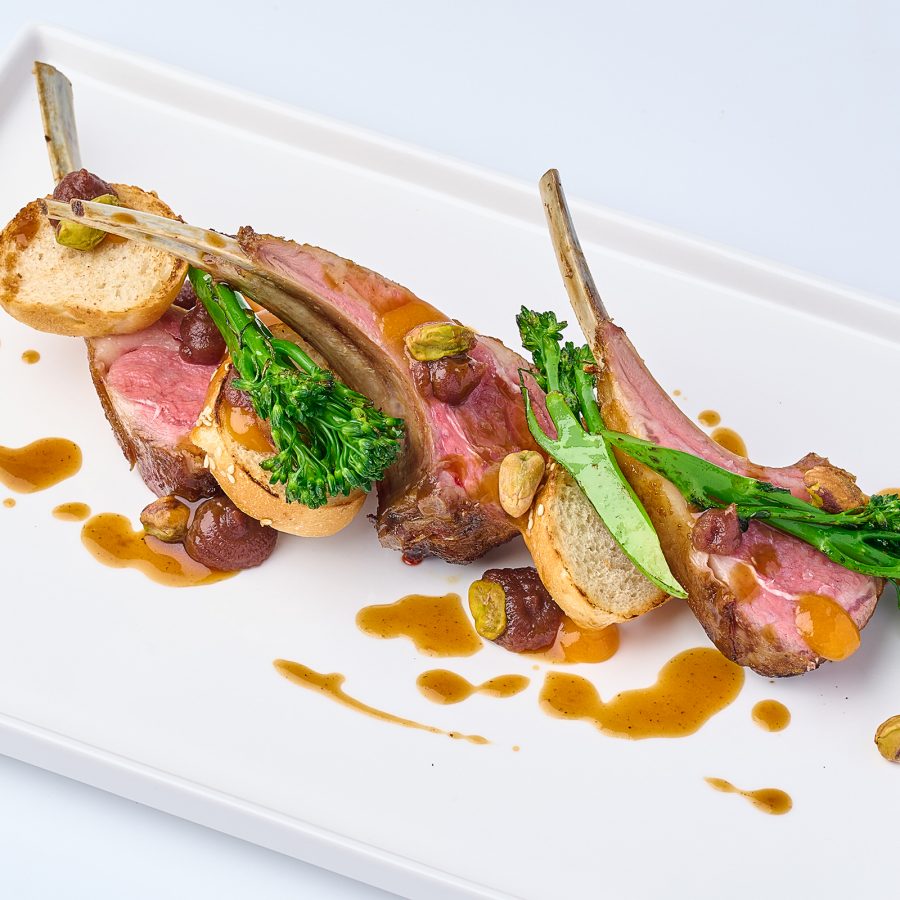 New Zealand lamb rack served on a white plate with greens at Indigo, George Town.
