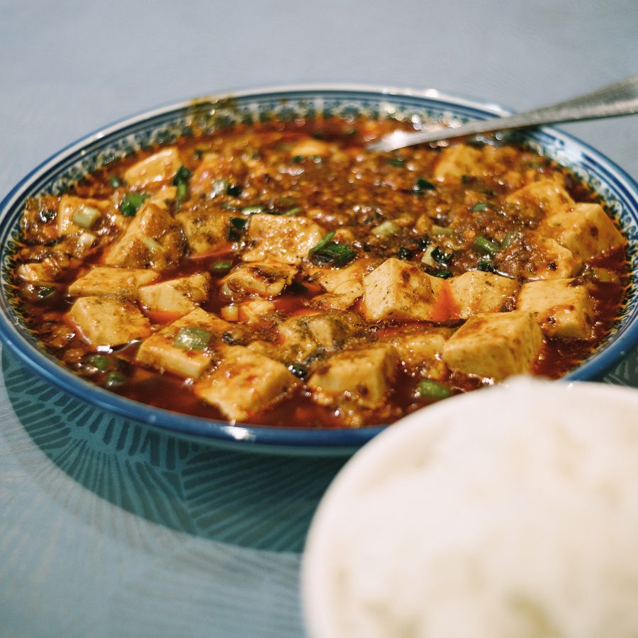 A dish of mapo tofu with a silver spoon and a bowl rice in the corner, served at Sijie in Causway Bay, Hong Kong.