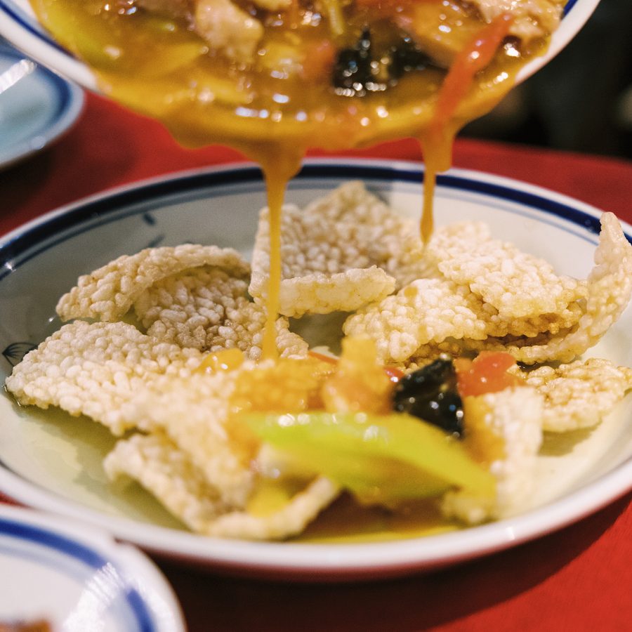 A closeup of a bowl of thick sauce being poured over a plate of rice crackers at River Sichuan in Sai Ying Pun, Hong Kong.