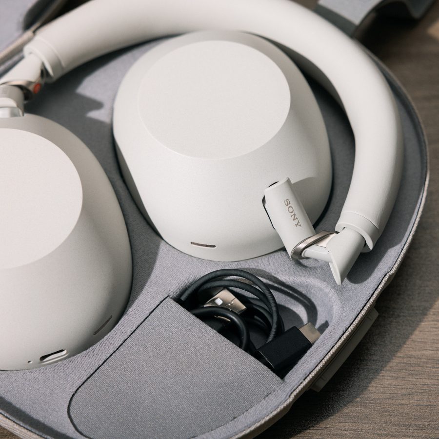 A pair of Sony WH-1000XM6 headphones in platinum silver inside their case, with cables in a separate pocket. 