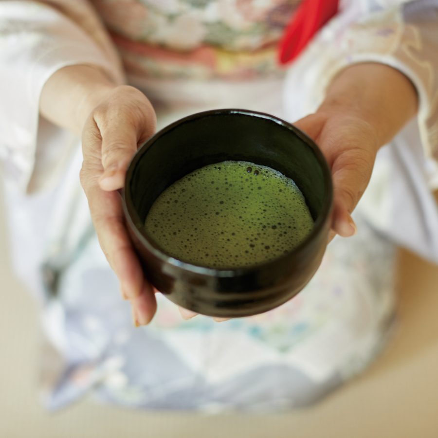 Close-up of hands holding a bowl of green tea. 